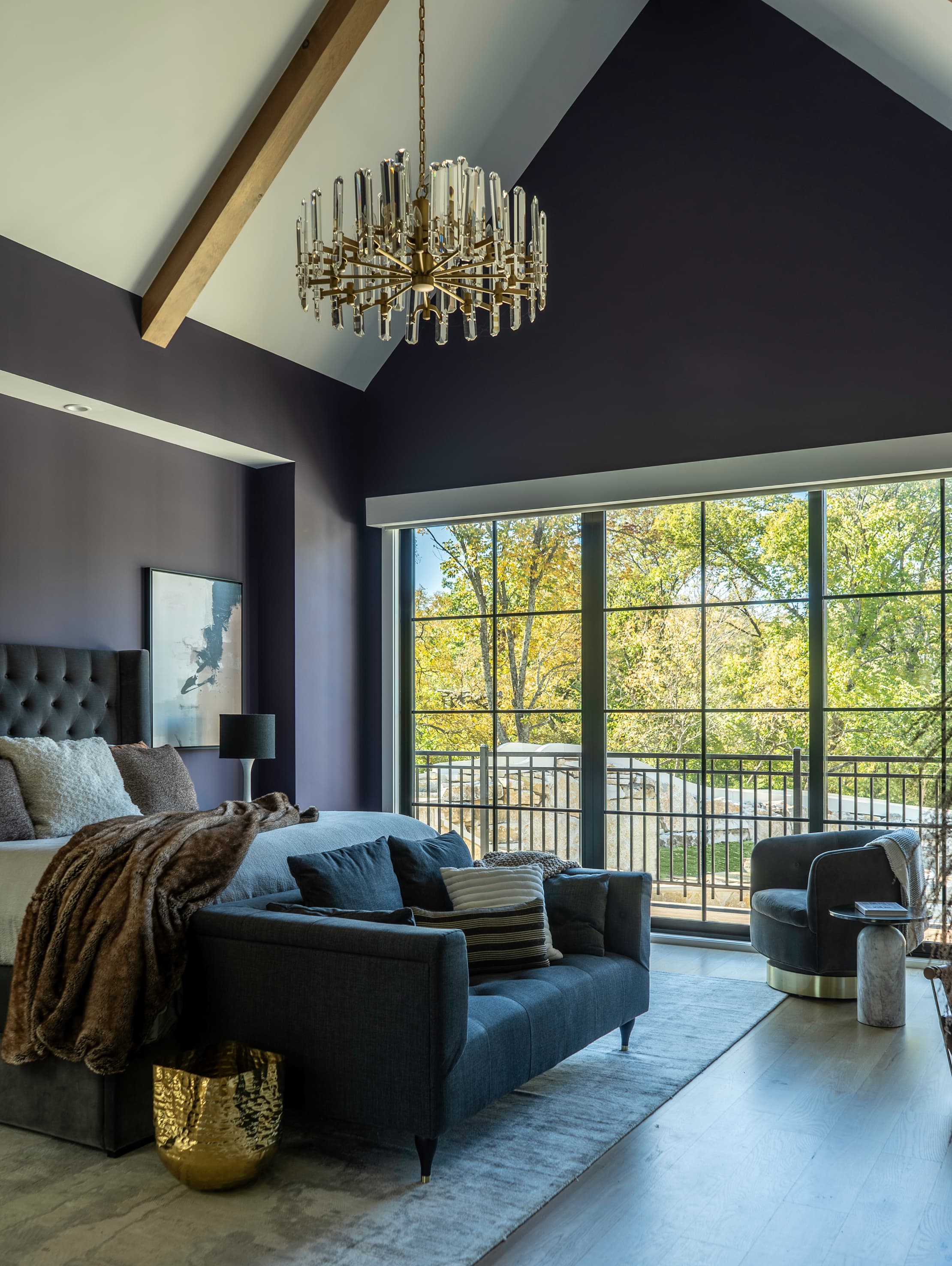 Primary suite, tufted headboard, sofa, swivel chair, crystal chandelier, charcoal violet walls