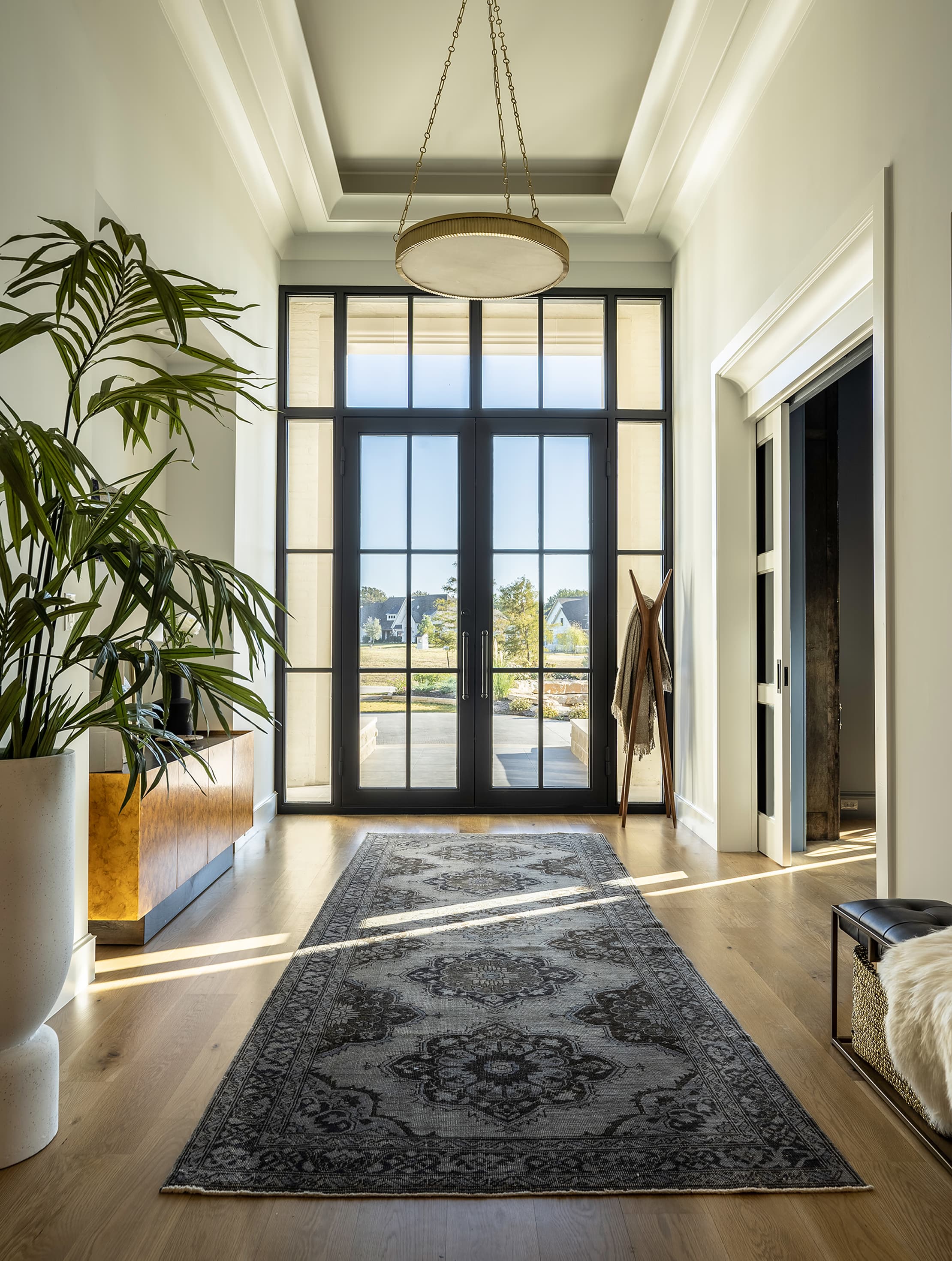 Vertical view straight through the foyer to the French doors with the brass chandelier overhead and the full vintage rug runner anchoring the floor