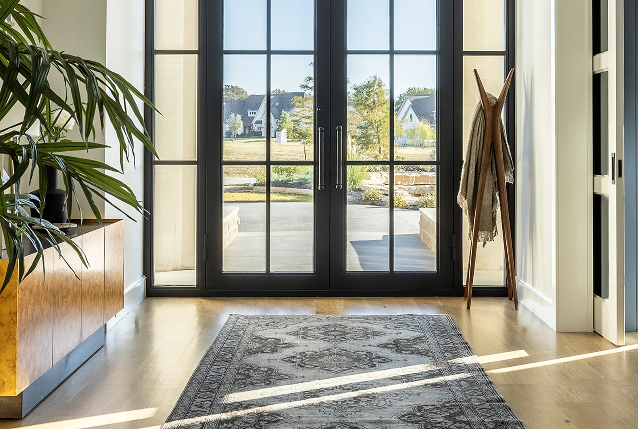 Horizontal architectural view of the entry: French doors at center, vintage rug runner, palm on the left, coat tree against the side wall