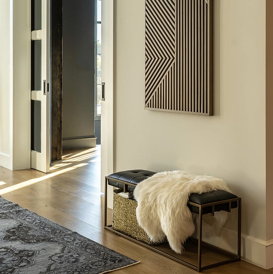 Tight detail of the black leather bench with a sheepskin throw, woven basket below, under the slatted wood geometric wall art
