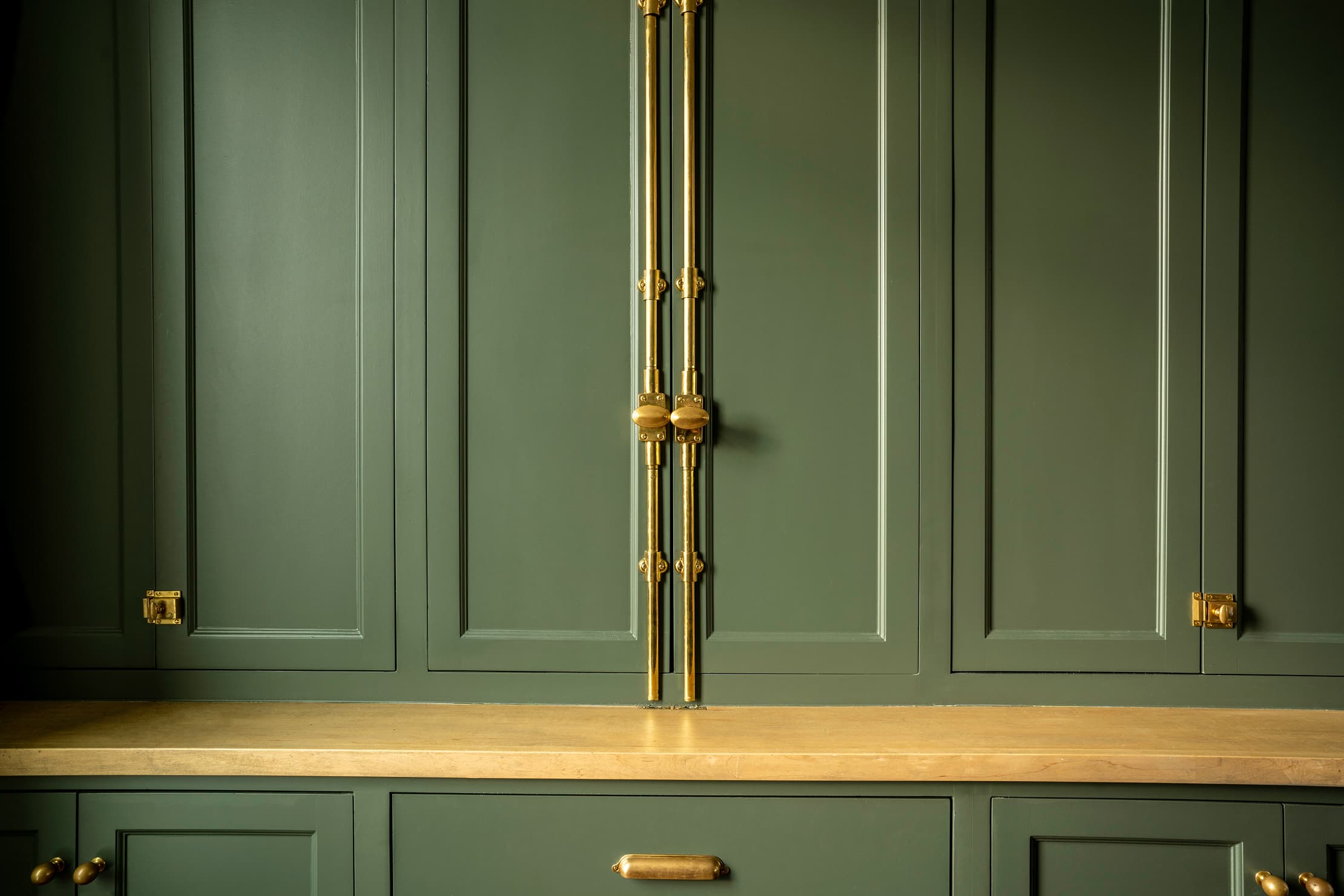Brass cremone bolt and cabinet hardware detail on sage green panels