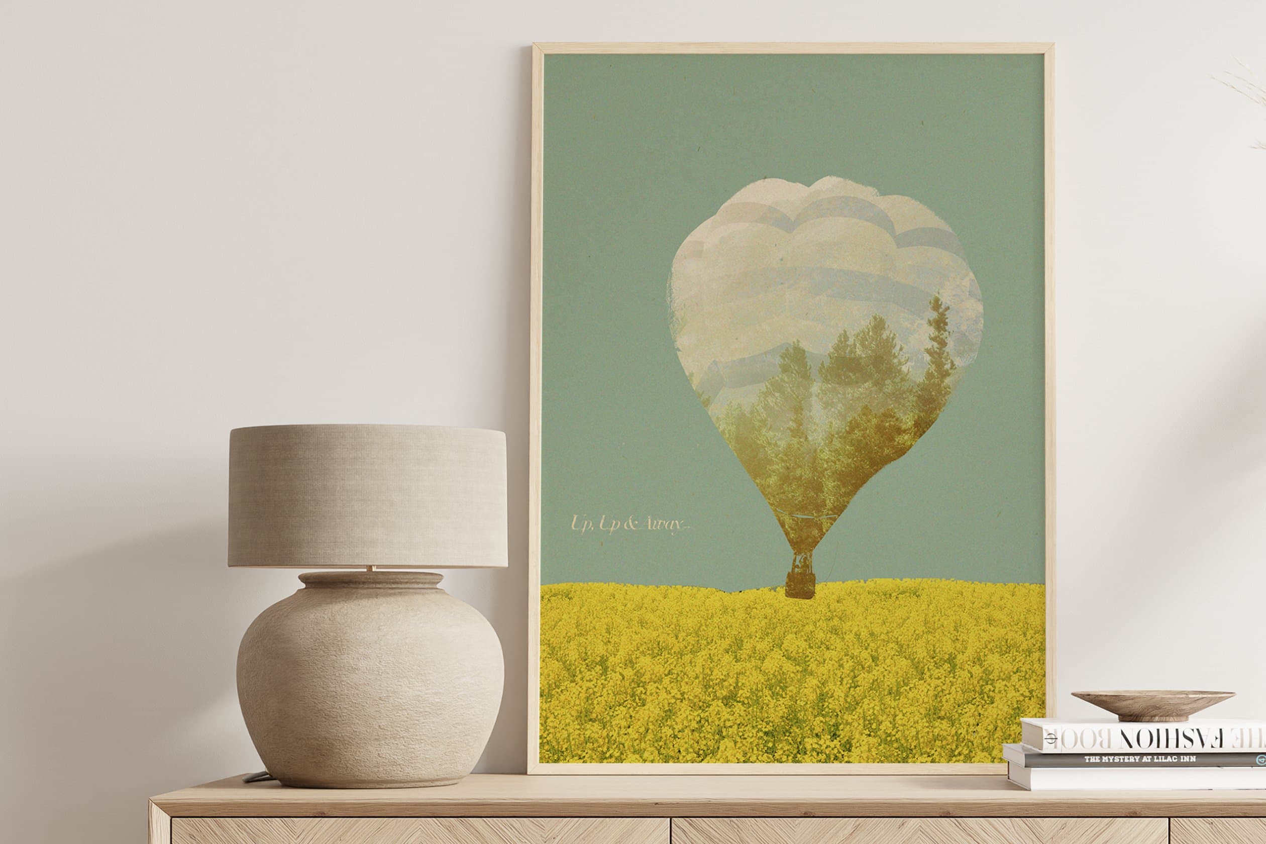 Up Up and Away poster, hot-air balloon double-exposed with trees over yellow rapeseed field, framed on console with lamp