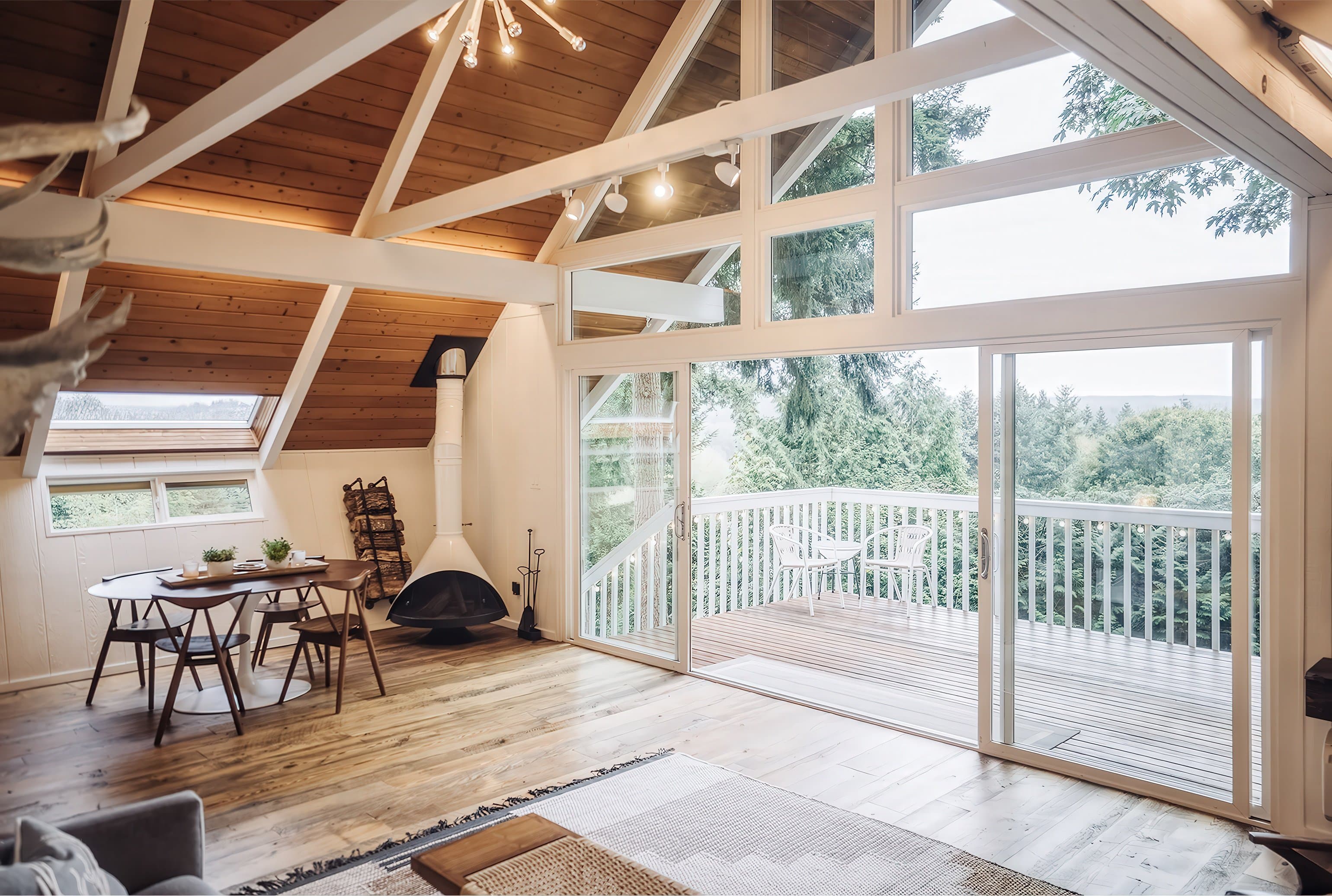 Mountain View chalet living room with A-frame ceiling, sputnik chandelier, Malm fireplace, walnut dining set, and 16-foot glass doors framing the Pacific Northwest tree canopy