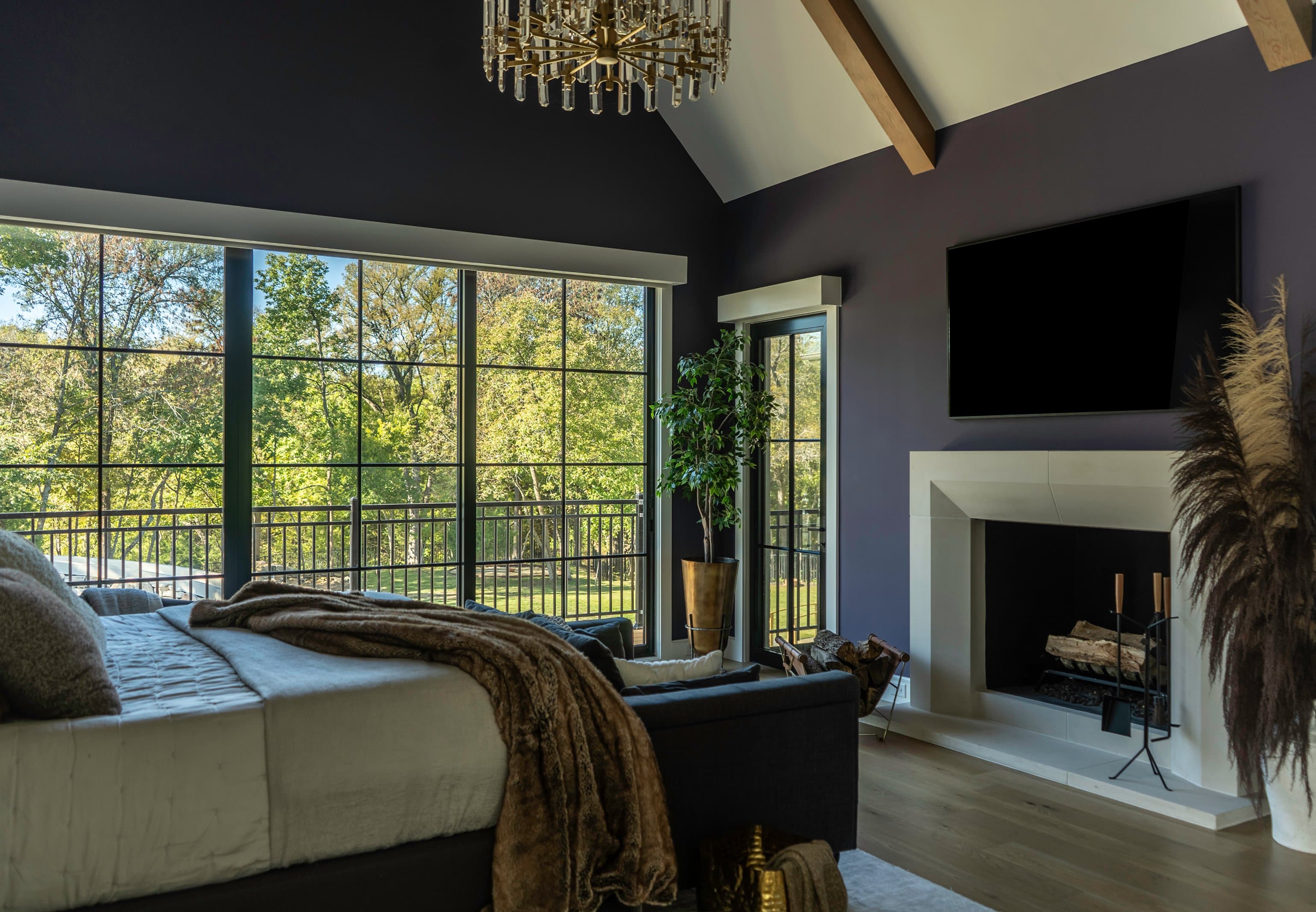 The Fairview primary suite, charcoal violet walls, crystal chandelier, cast stone fireplace, floor-to-ceiling windows