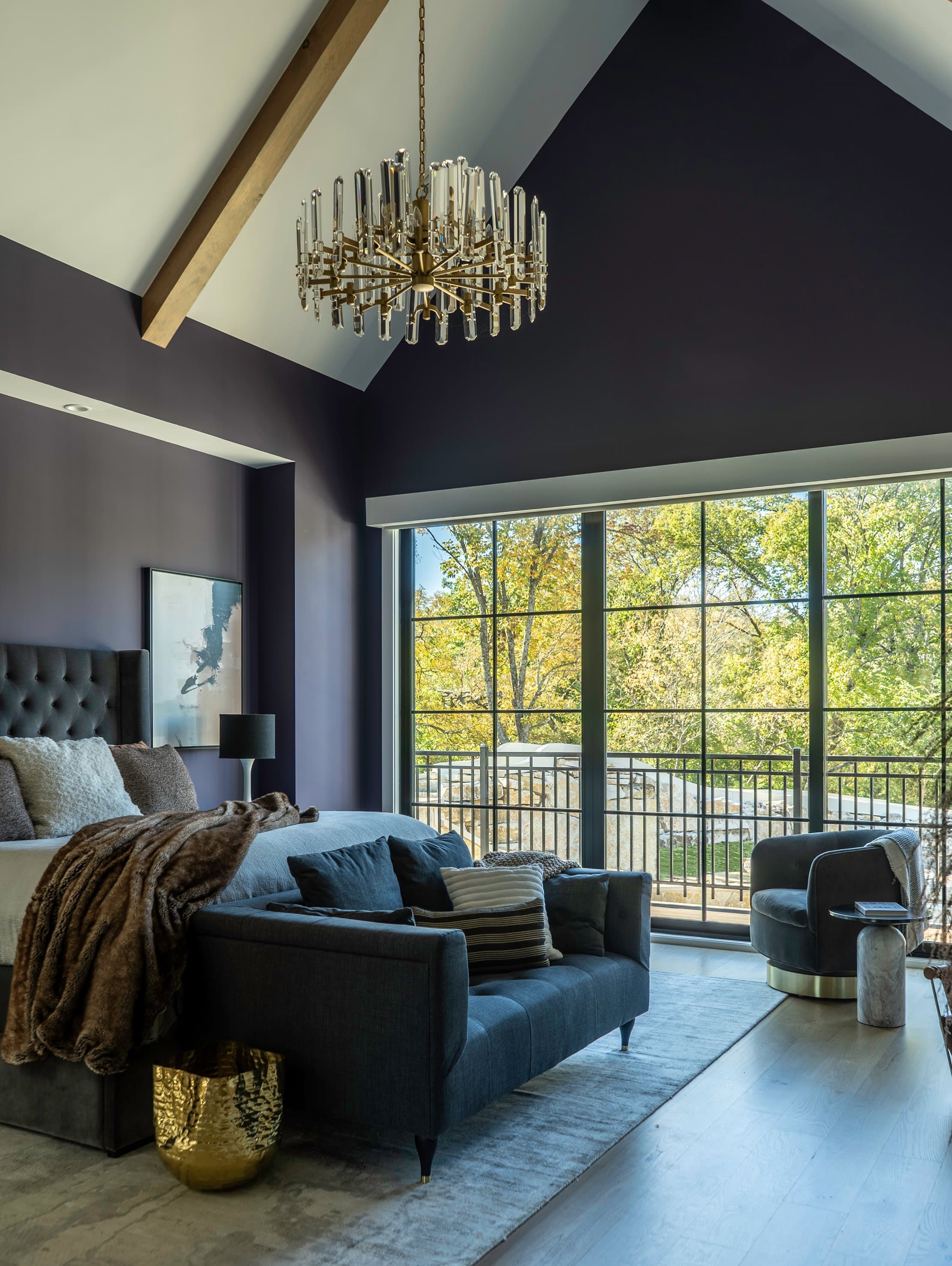 Primary suite, tufted headboard, sofa, swivel chair, crystal chandelier, charcoal violet walls