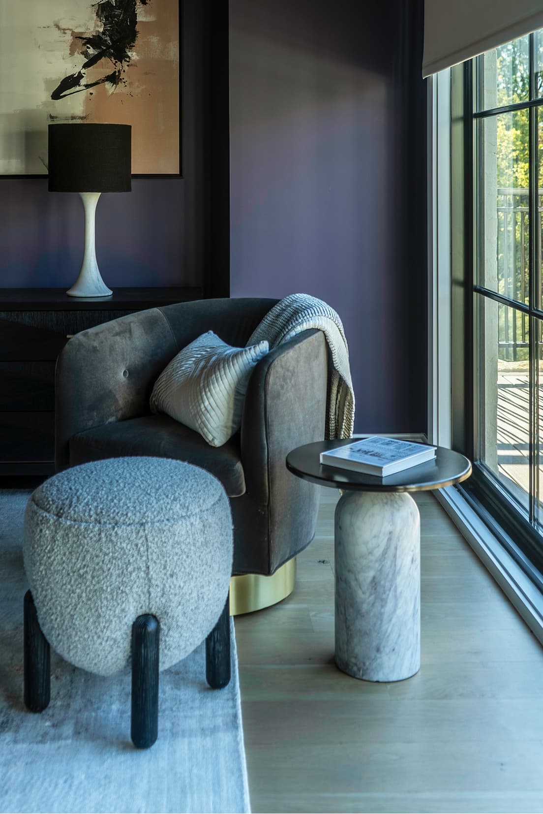 Reading corner, swivel chair with bouclé ottoman, marble pedestal table, charcoal violet walls