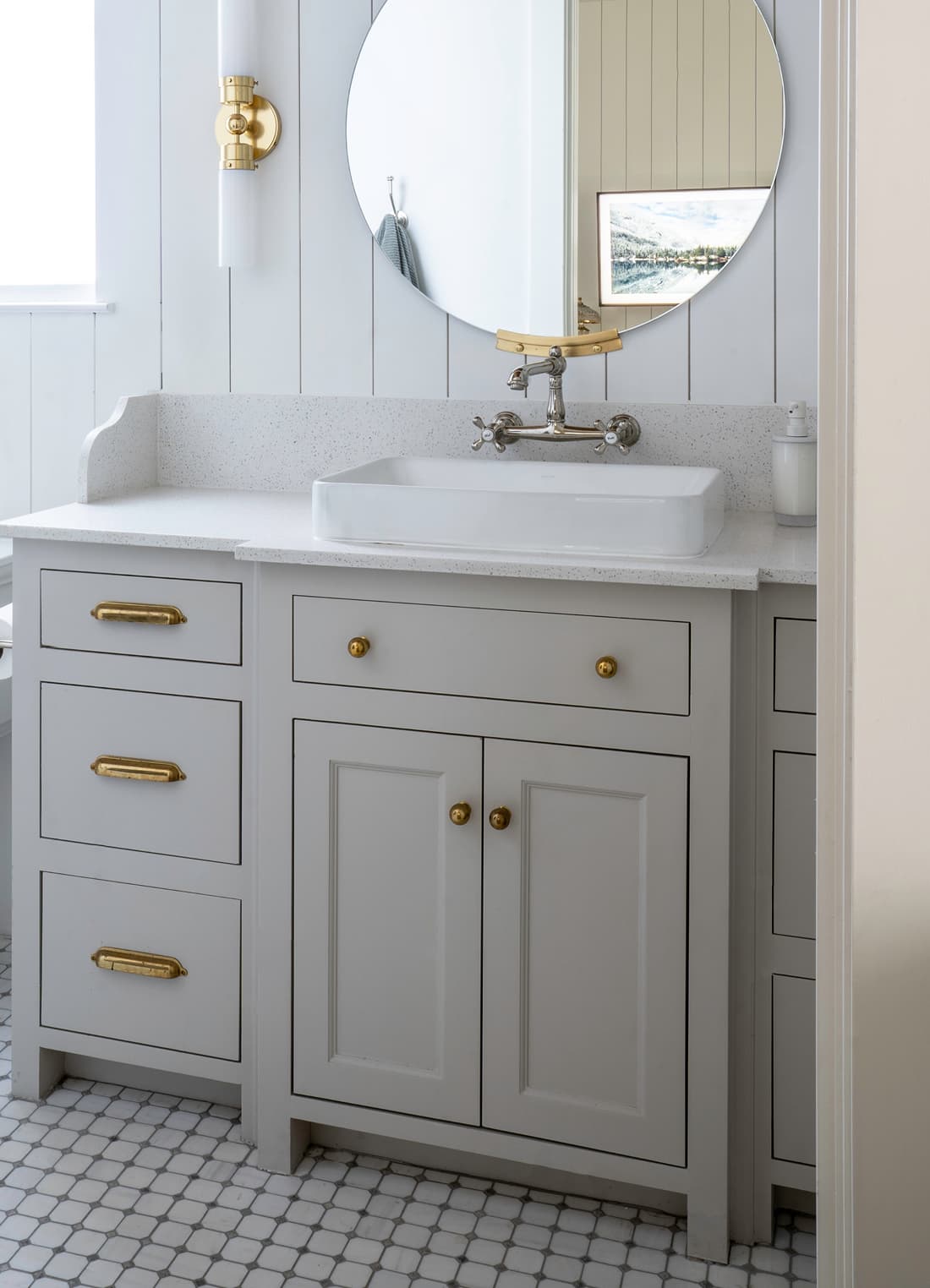 Modern farmhouse powder room with circular brass mirror, brass cabinet pulls, brass sconce, vessel sink, and patterned hex floor tile