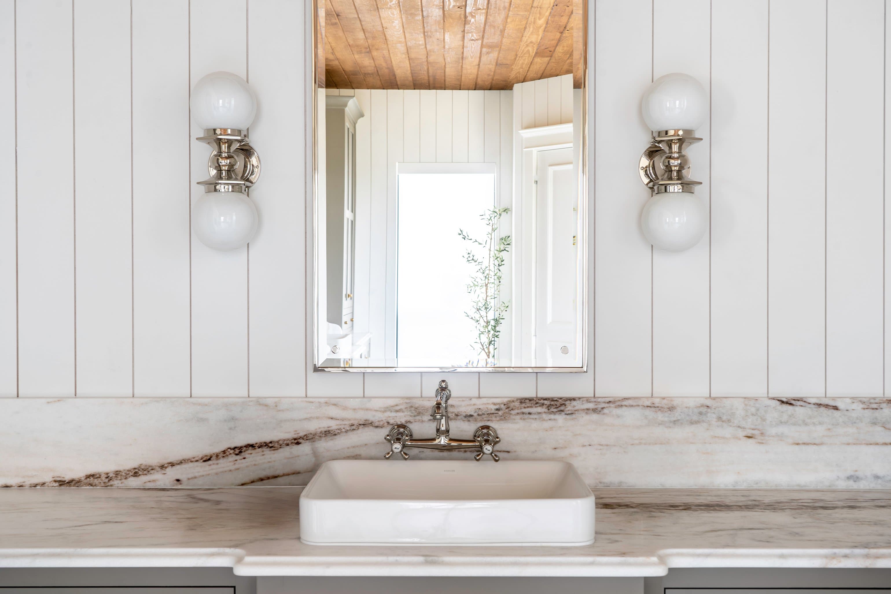 Modern farmhouse vanity with vertical shiplap walls, reclaimed wood ceiling, marble counter, polished nickel sconces, and brass-framed mirror