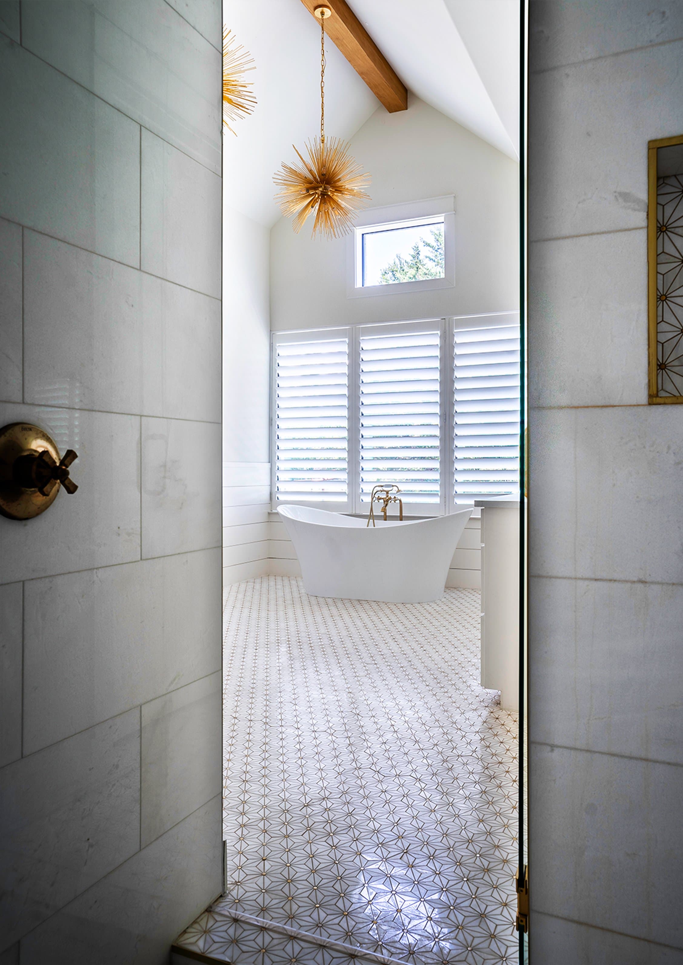 Quiet glam primary bath with veined marble walls, freestanding tub, brass urchin chandelier, and patterned floor tile
