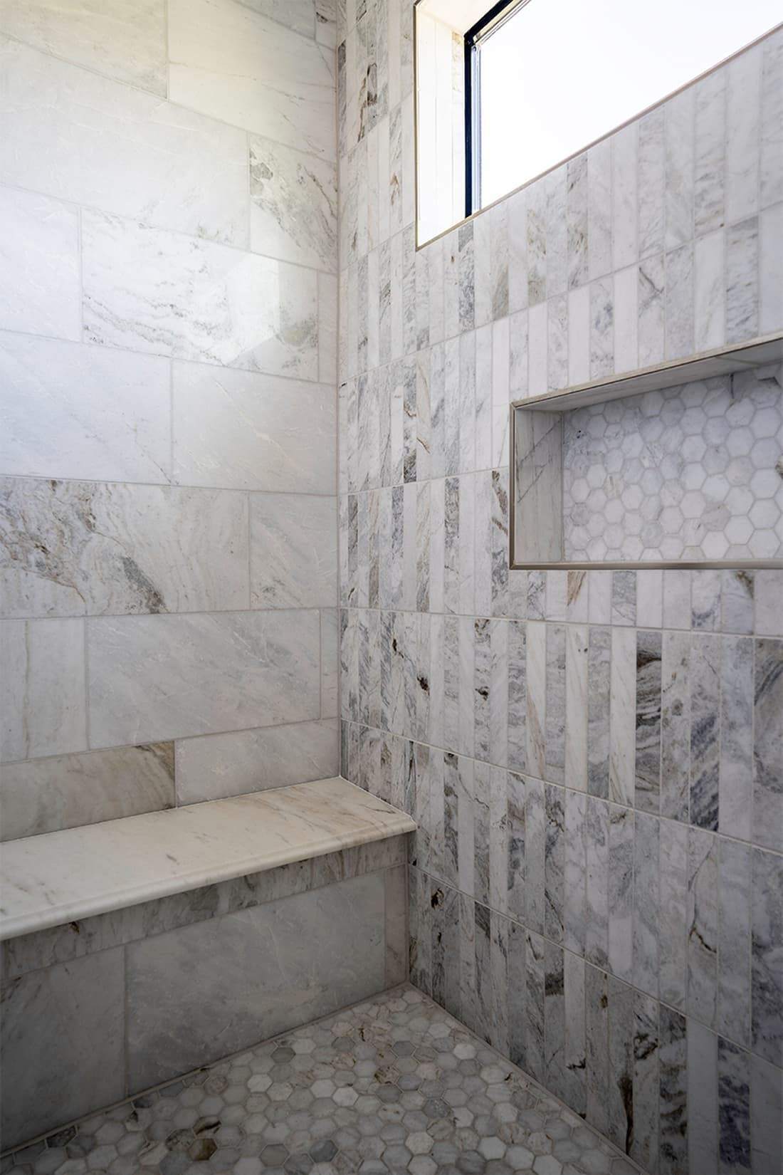 Urban southwest marble shower with vertical stacked tile, recessed niche with hexagon detail, marble bench, and clerestory window