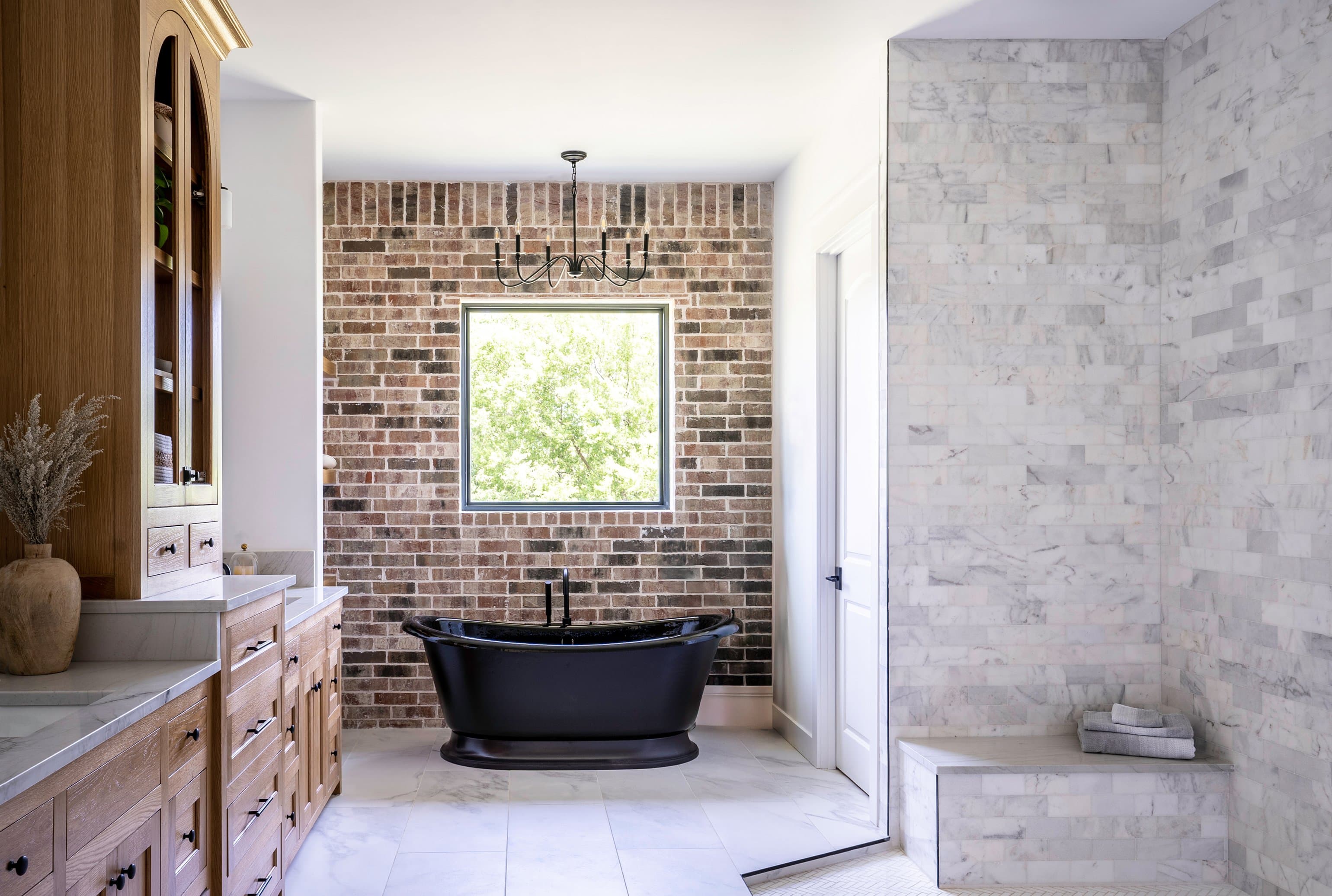 Urban southwest primary bath with exposed brick wall, matte black freestanding soaking tub, white oak vanity, and marble shower