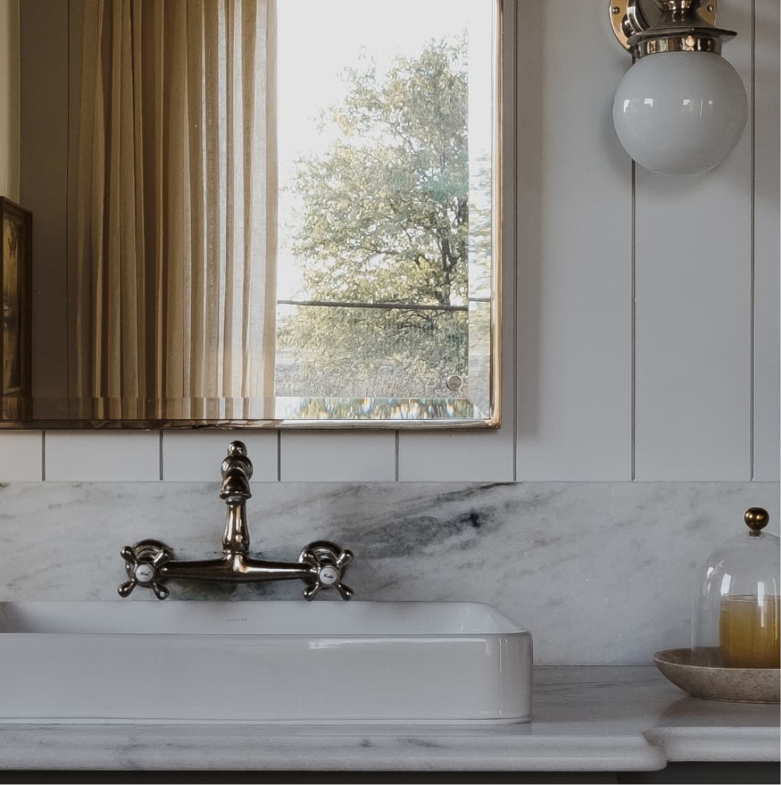Detail, cross-handle wall faucet, marble backsplash, globe sconce, window reflection