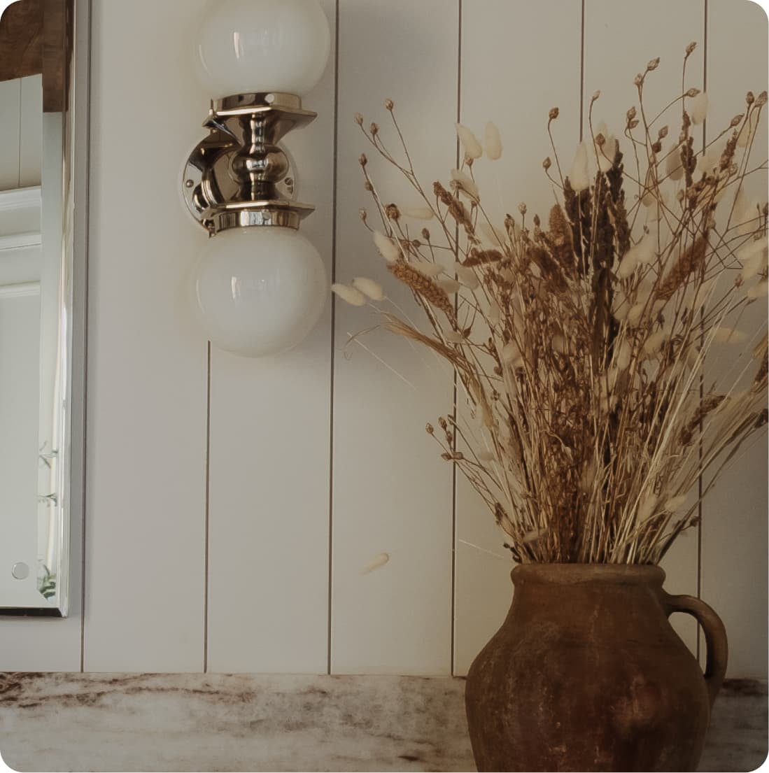 Detail, polished nickel double globe sconce, dried botanicals in clay pot on marble