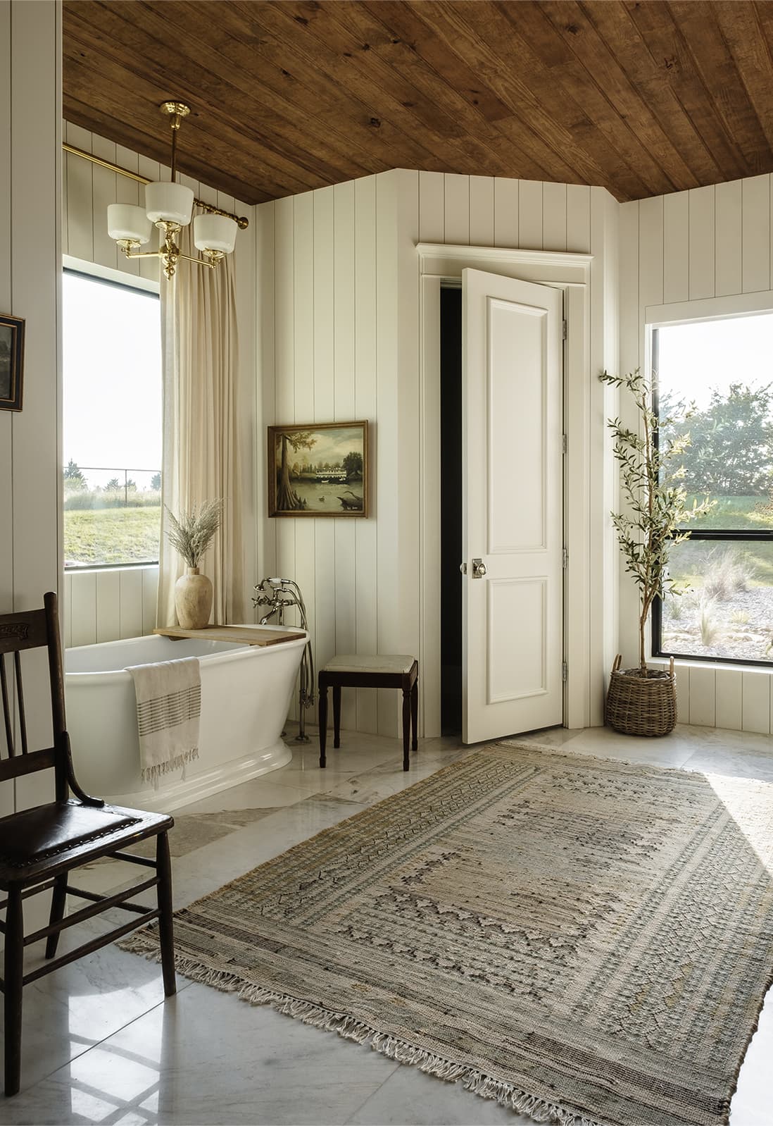 Freestanding tub beneath wood plank ceiling, landscape painting, oriental rug, natural light