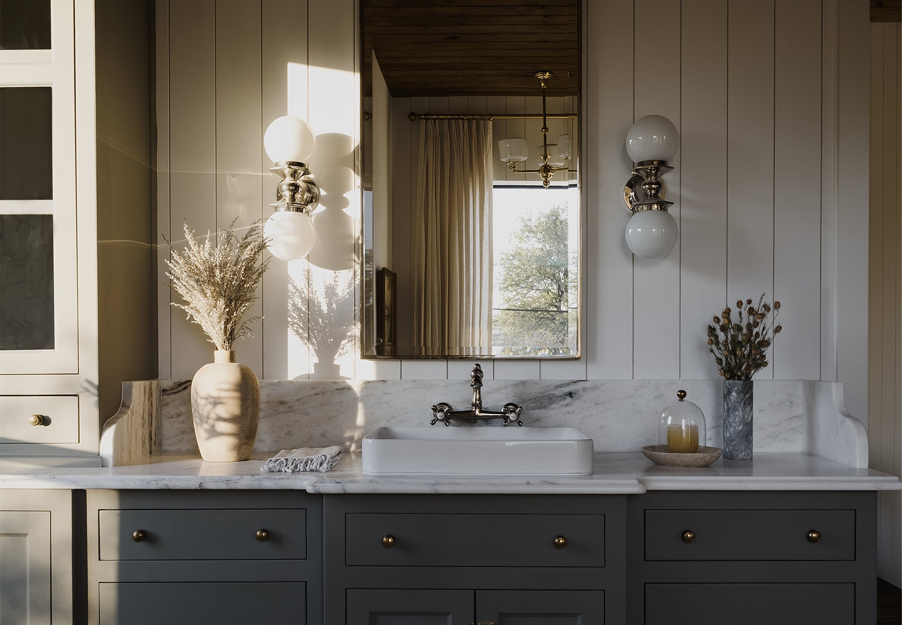 Hill Country primary bath, marble vanity with globe sconces, sage cabinetry, dried botanicals