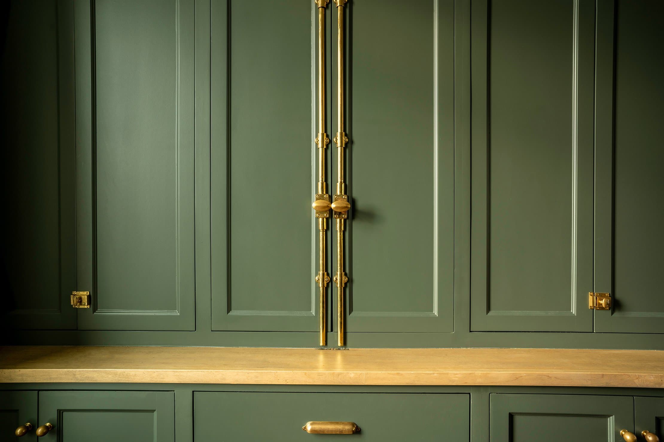 Brass cremone bolt and cabinet hardware detail on sage green panels