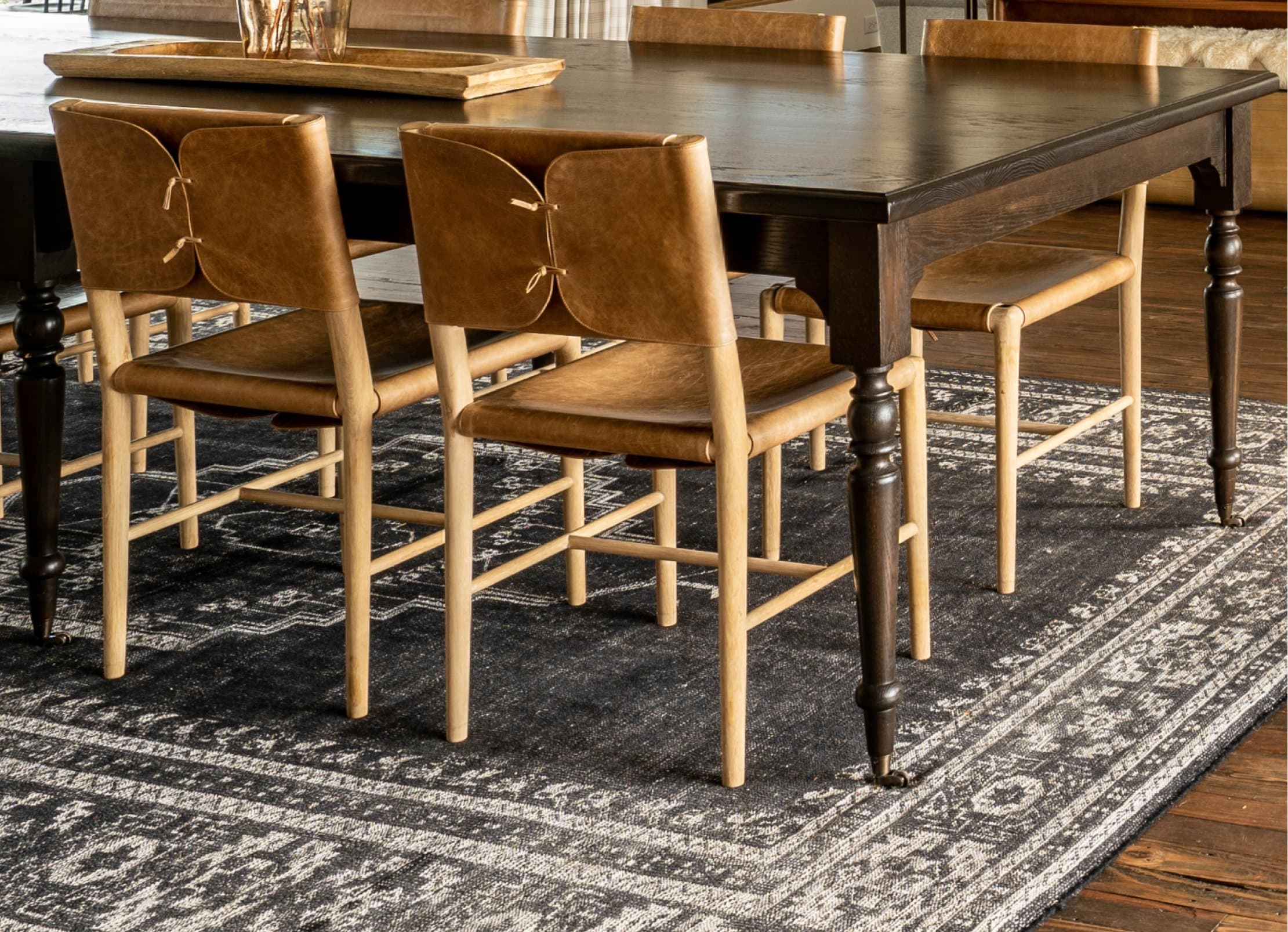Full dining table with leather safari chairs on dark patterned rug