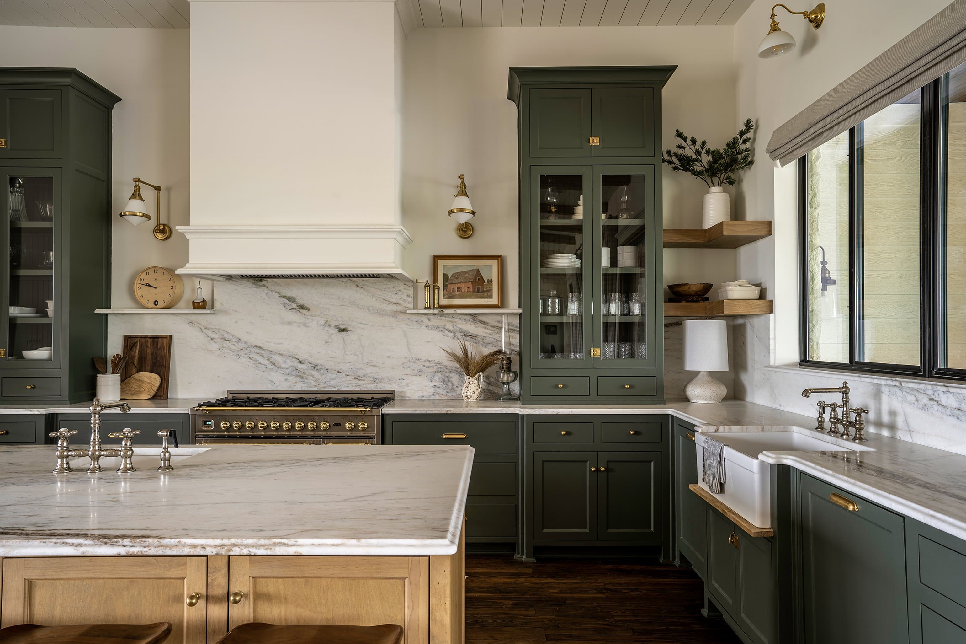 Marble backsplash detail with brass sconces, farmhouse sink, sage green cabinetry