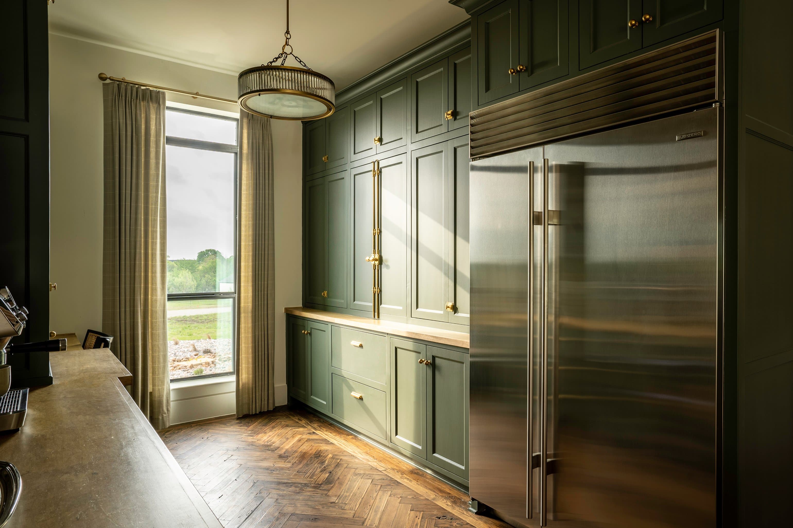 Pantry wall with sage green floor-to-ceiling cabinetry, stainless refrigerator, pendant light