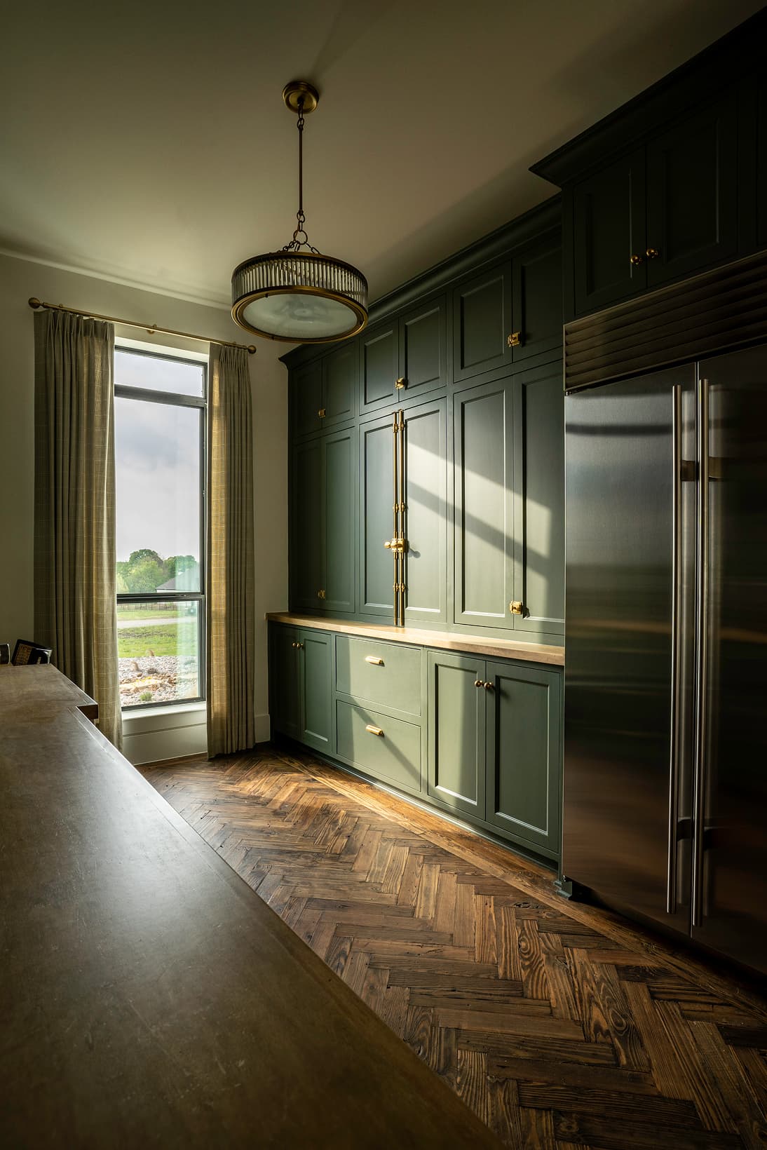 Pantry wall with sage green cabinetry, herringbone floor, pendant light