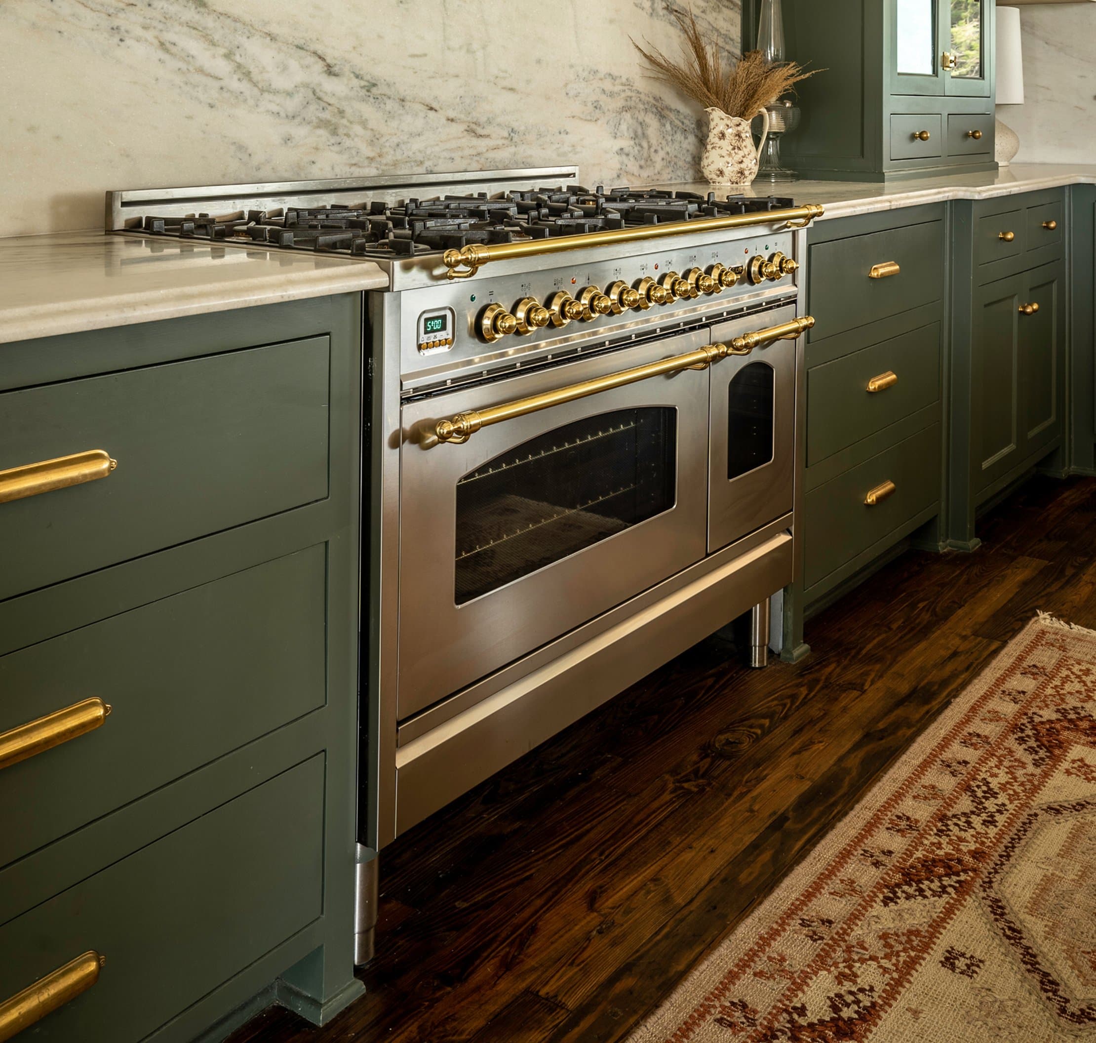 Professional range with brass knobs, marble backsplash, sage green cabinetry