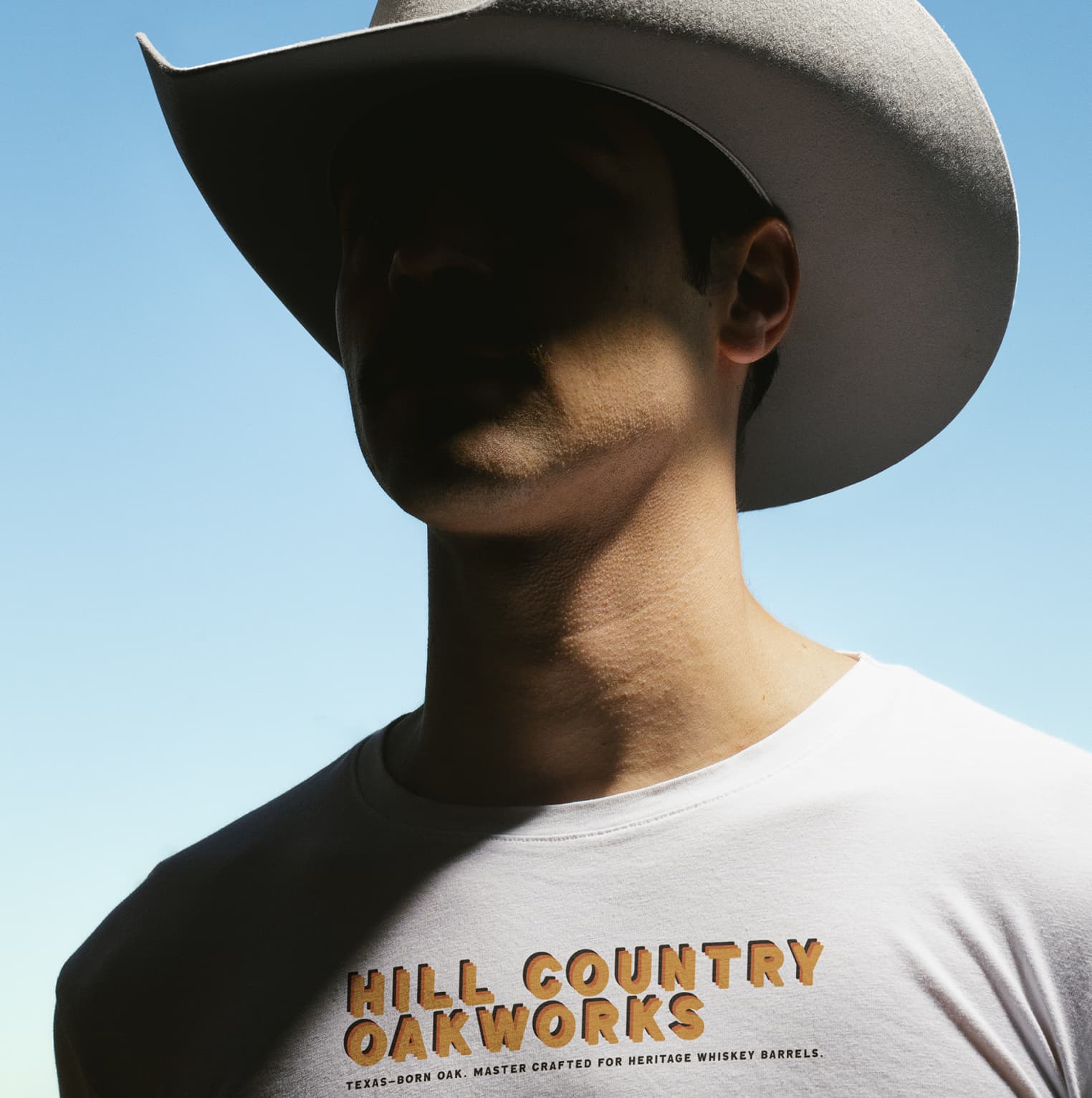 Portrait of a cowboy-hat-wearing man in a HILL COUNTRY OAKWORKS branded t-shirt with the brand tagline below