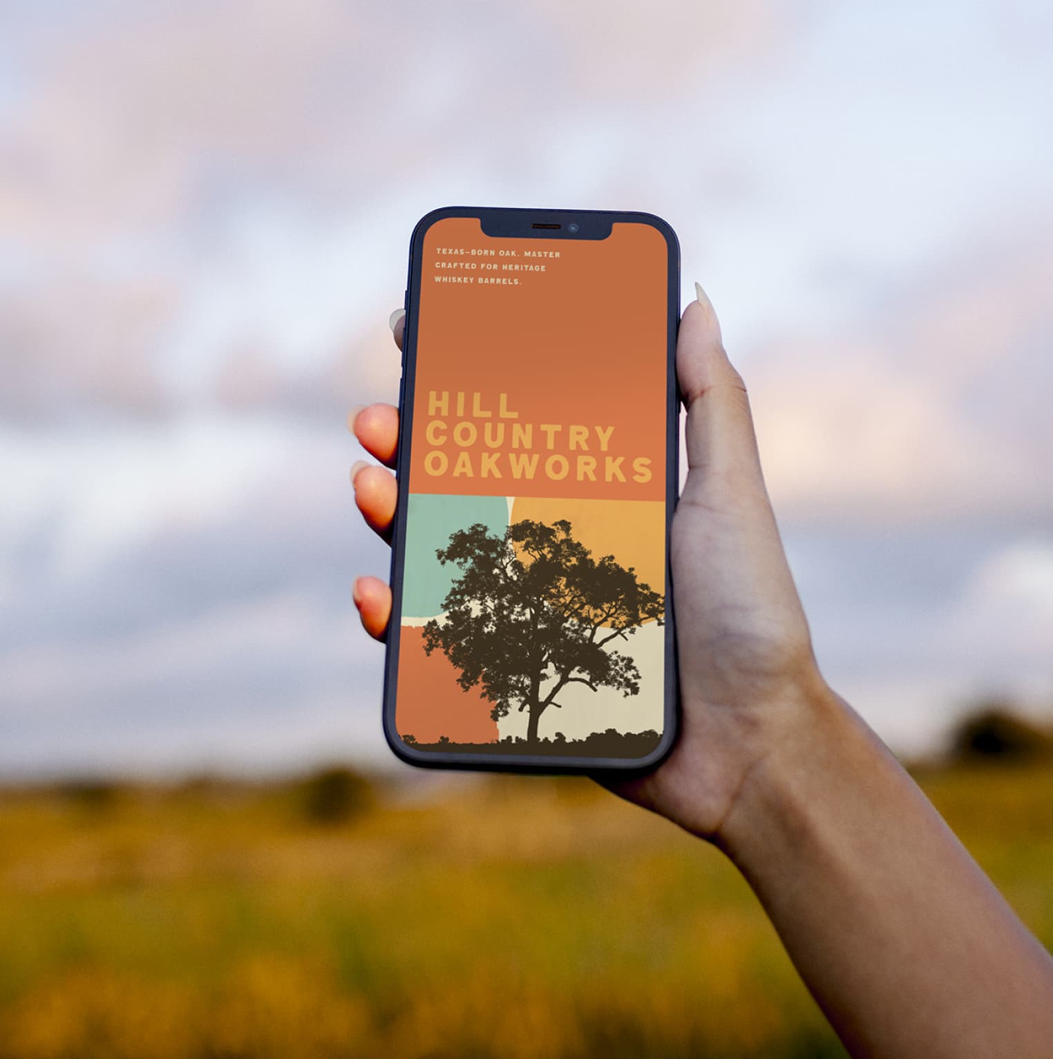 iPhone mockup showing the Hill Country Oakworks poster on the lock screen, hand-held against an open Texas sky