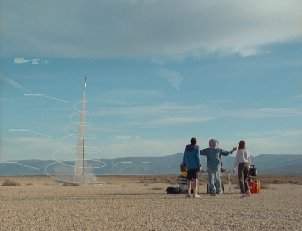 Mother x Anthropic film still, three figures watching a model rocket launch in the desert