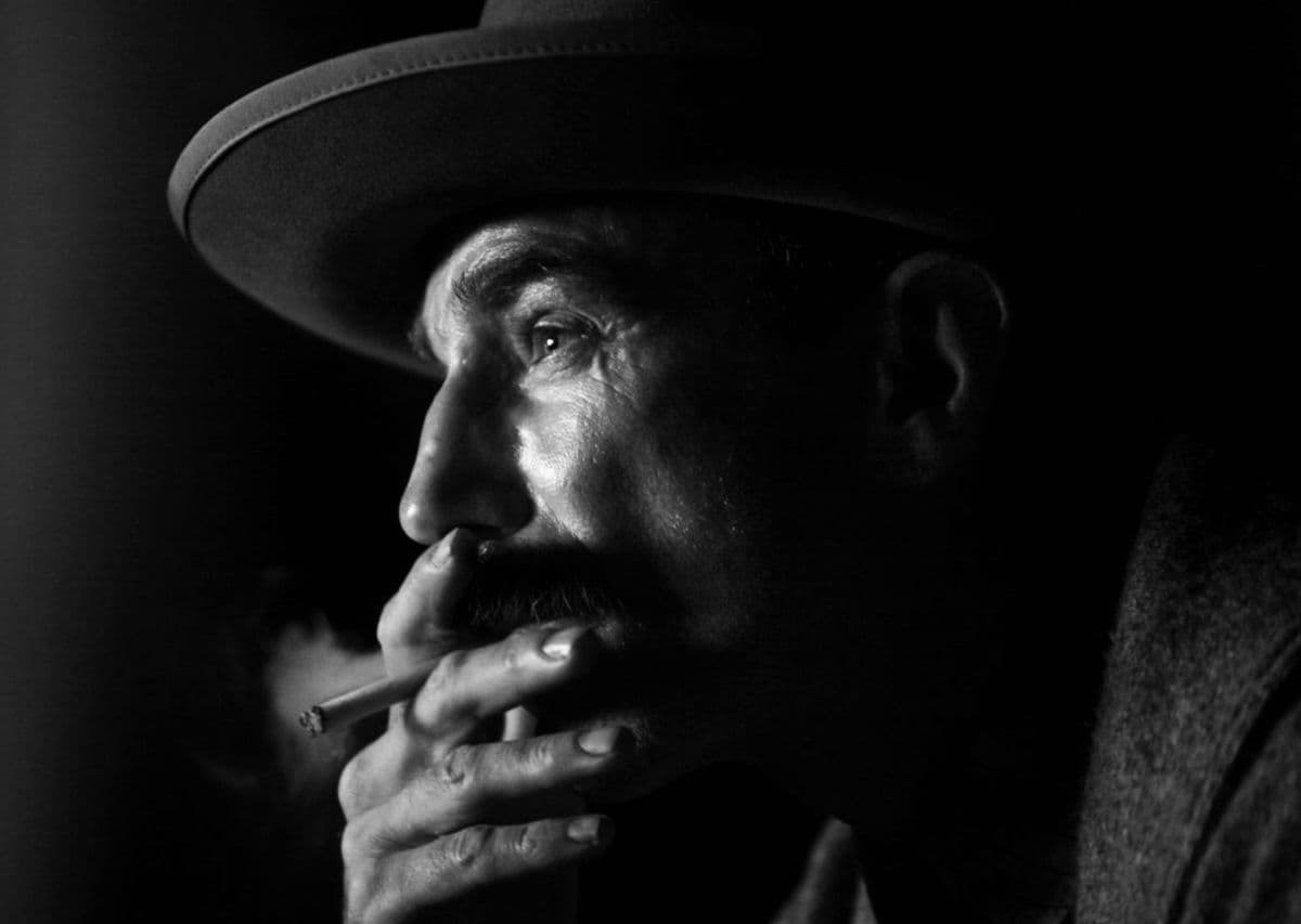 Black-and-white cinematic close-up, man in wide-brim hat smoking a cigarette