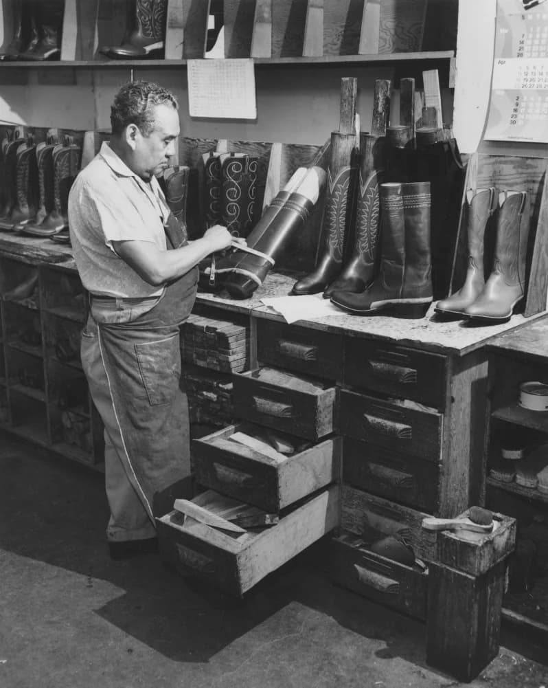 Black-and-white photo of a cowboy boot maker shaping leather over wooden lasts