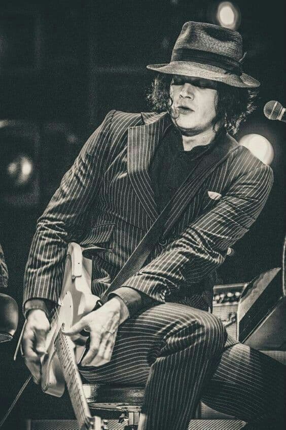 Black-and-white live shot, man in pinstripe suit and fedora playing electric guitar
