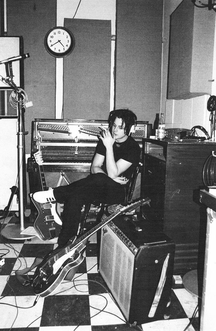 Black-and-white portrait, Jack White in studio with upright piano and Jaguar guitar