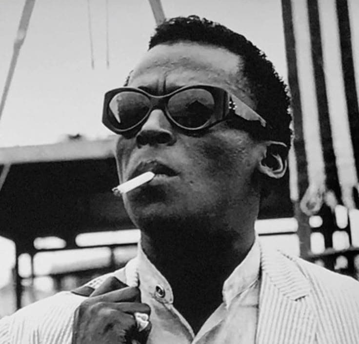 Black-and-white portrait of Miles Davis in cat-eye sunglasses with a cigarette