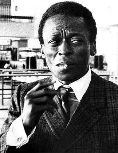 Black-and-white portrait of Miles Davis in tweed suit smoking a cigarette
