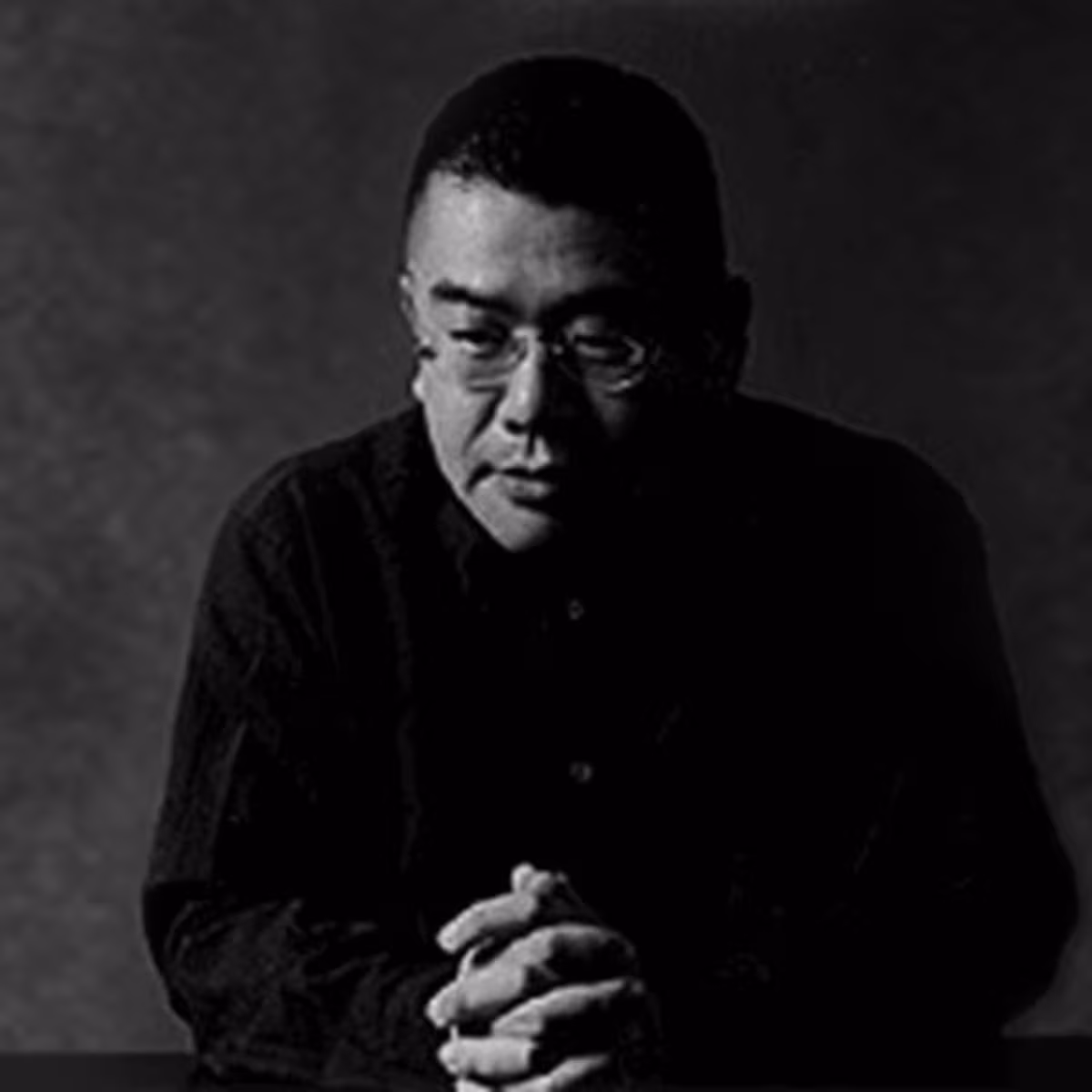 Black-and-white portrait of a man in glasses with hands clasped in front of him