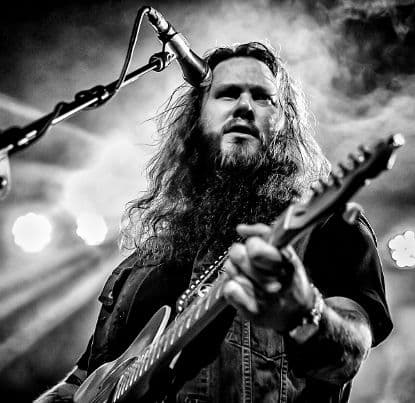 Black-and-white live shot, long-haired singer with electric guitar in stage spotlights
