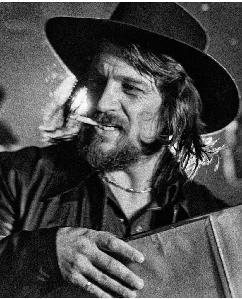 Black-and-white portrait of Waylon Jennings in cowboy hat carrying a portfolio