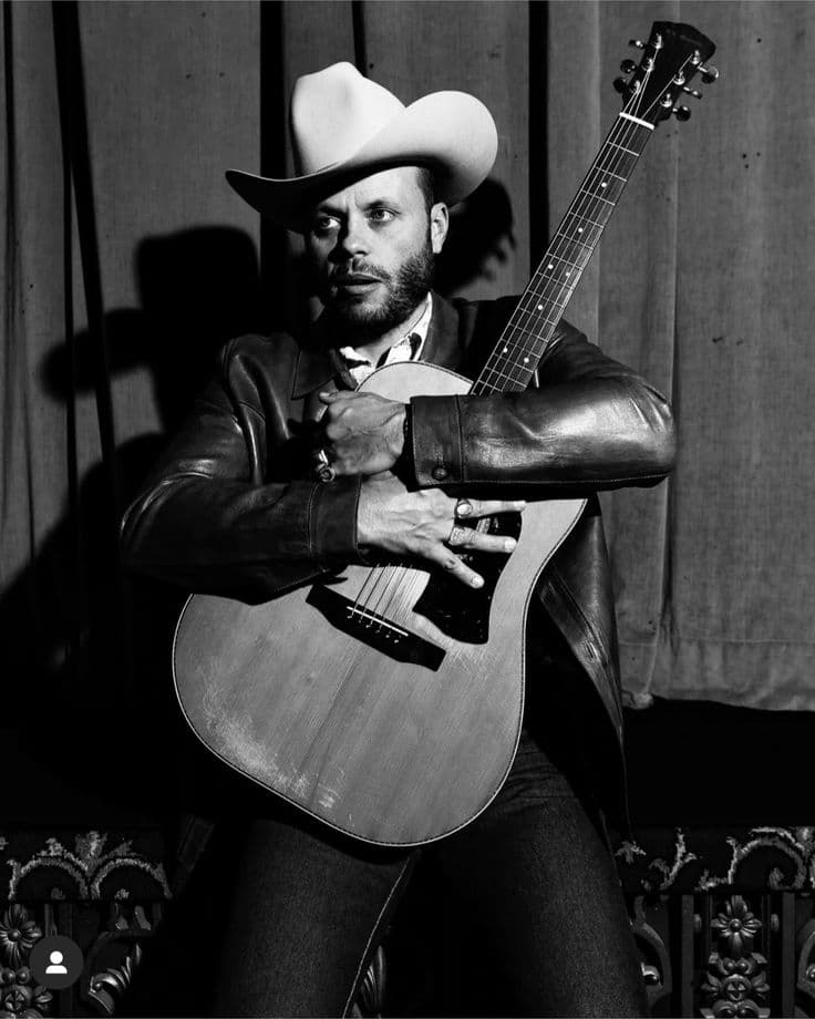 Country singer in cowboy hat and leather jacket holding an acoustic guitar