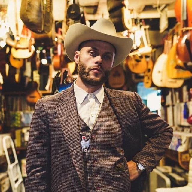 Country singer in cowboy hat and tweed suit standing inside a hanging-guitar shop