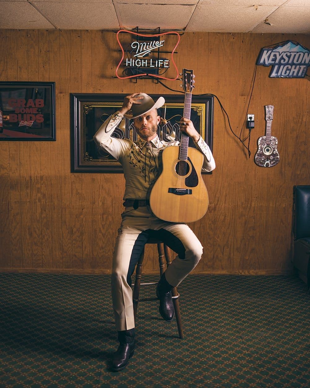 Country singer in cowboy hat with acoustic guitar, Miller High Life neon sign behind