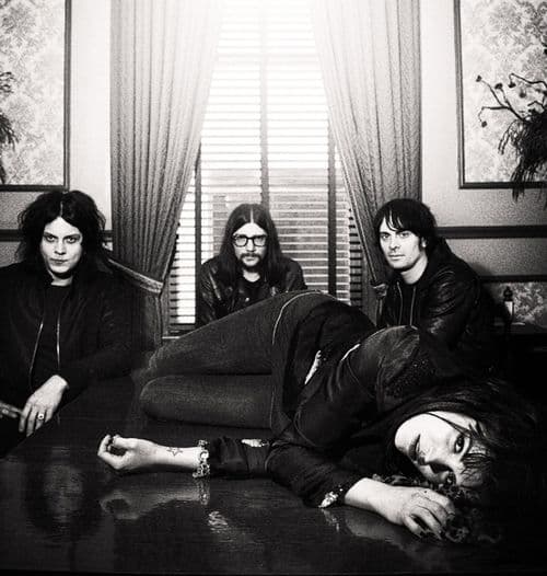 Black-and-white band portrait, four musicians in an ornate floral-walled room