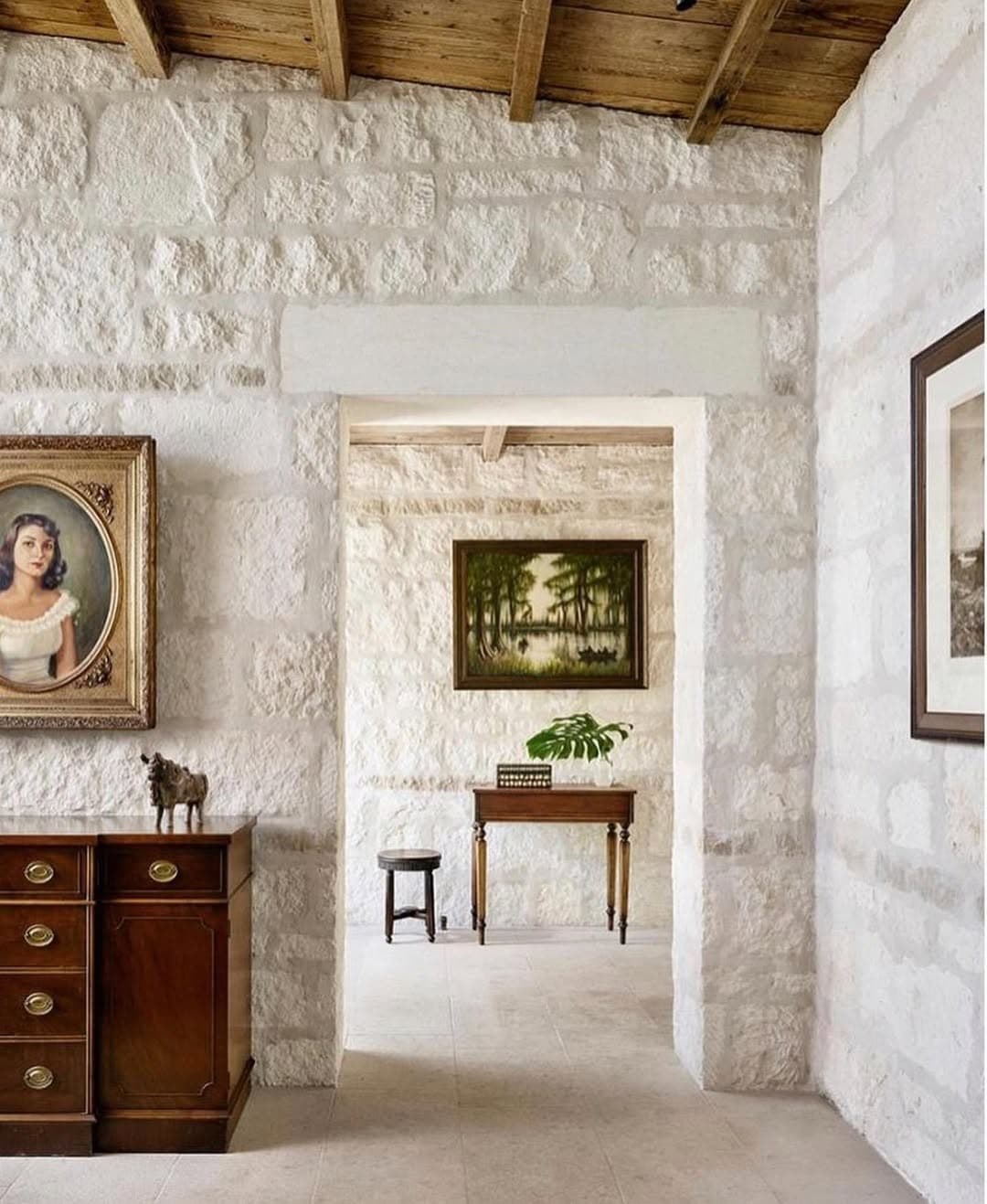 Texas Hill Country stone foyer with antique portrait, dark wood console, and a monstera leaf