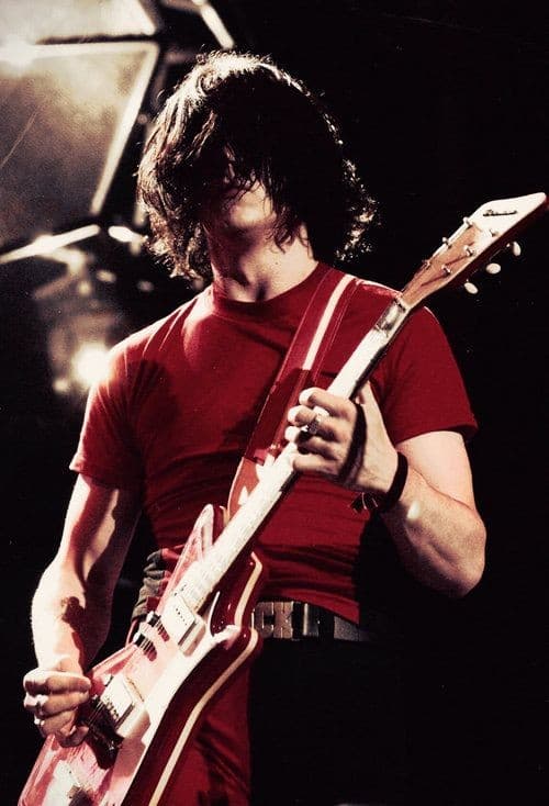 Jack White on stage in red shirt with red electric guitar