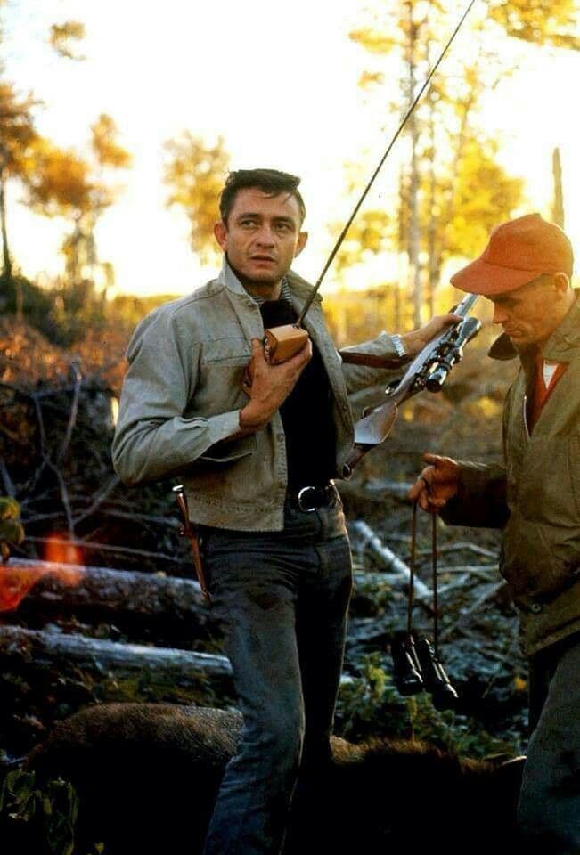 Johnny Cash holding a transistor radio outdoors in fall, hunter beside him with a rifle