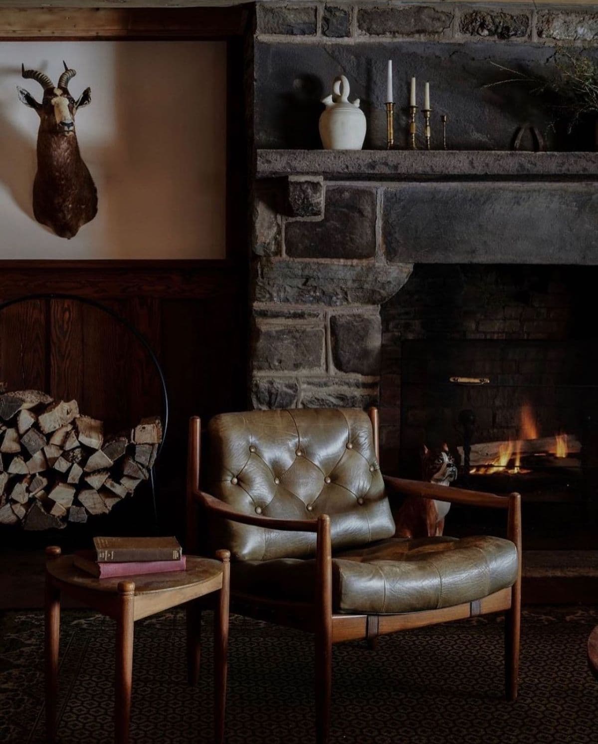 Olive leather button-tufted chair beside a stone fireplace with mounted antelope head
