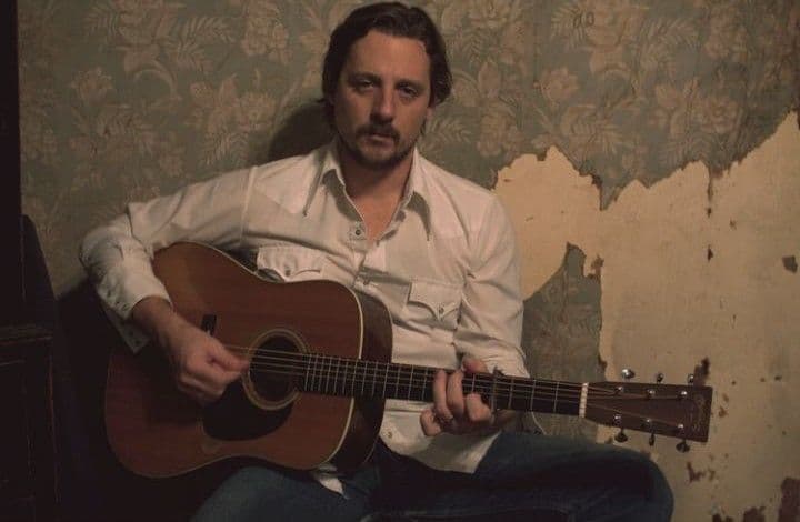 Musician with acoustic guitar against peeling vintage floral wallpaper