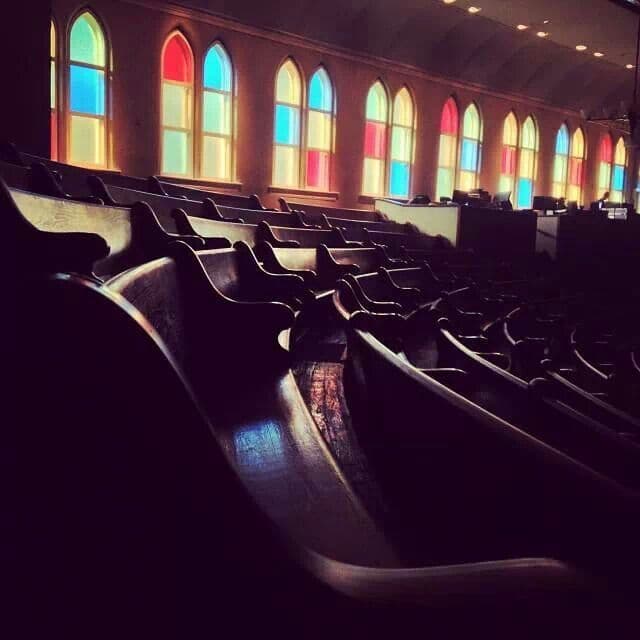 Empty Ryman Auditorium pews with stained-glass arched windows in primary colors