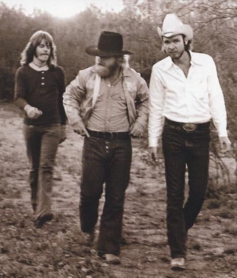 Sepia photograph, three cowboys walking down a dirt road