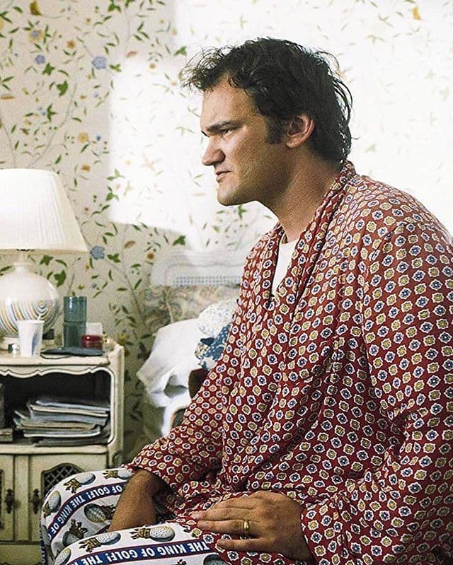 Quentin Tarantino in a printed silk robe seated in a floral-wallpapered bedroom