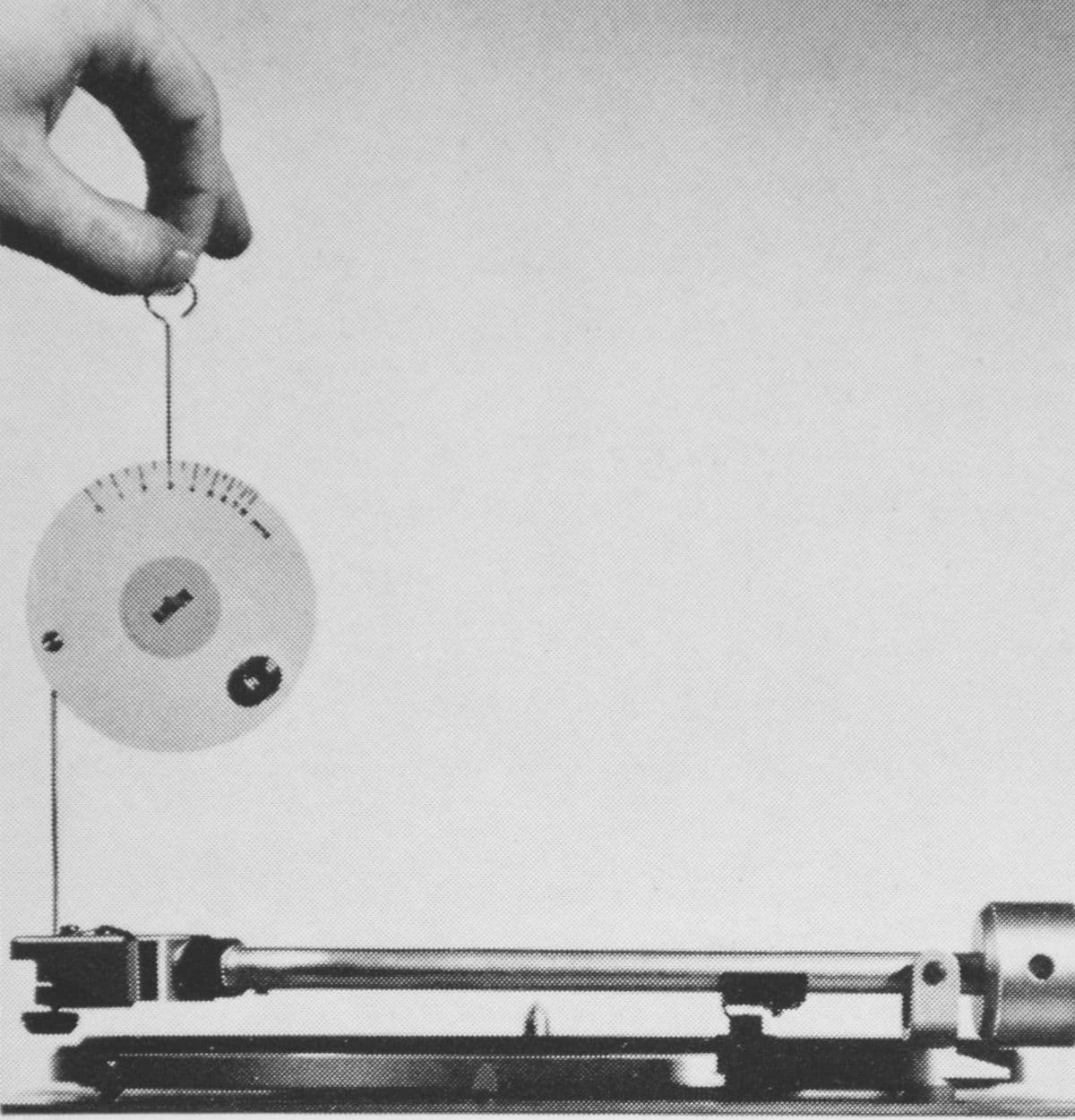 Vintage black-and-white photo, hand using a stylus pressure gauge on a turntable